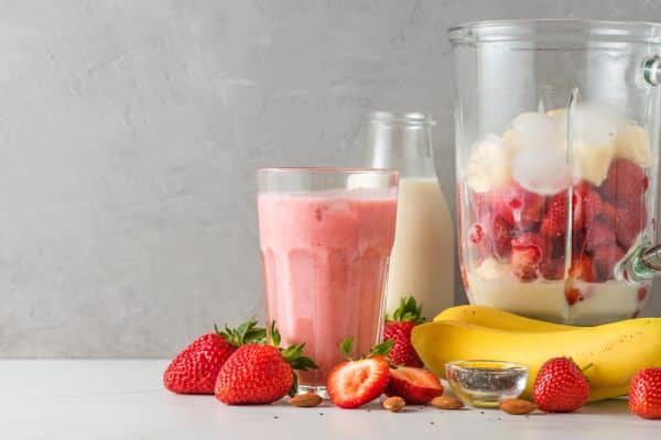Glass strawberry and banana smoothie or milkshake with fresh juicy ingredients in blender for making healthy drink